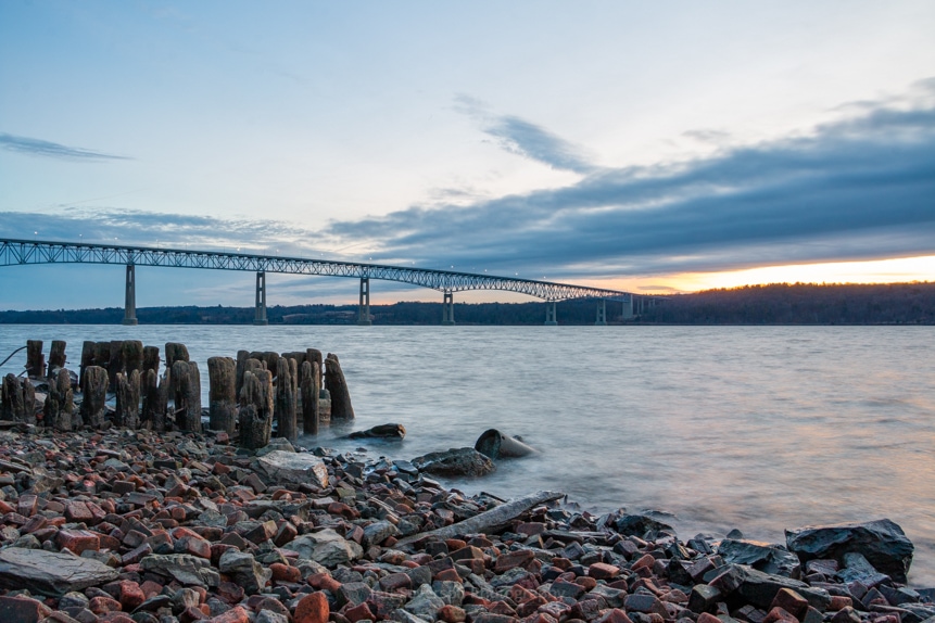 A photo of the Kingston-Rhinecliff Bridge and the wood pilings along the shores of the Hudson River at Charles Rider Park at sunrise on a January morning.