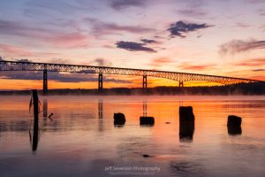 A photo of moorings from an old pier silhouetted on the Hudson River during sunrise.