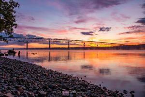 A photo of sunrise breaking over the Kingston-Rhinecliff Bridge from along the Hudson River at Charles Rider Park in Kingston, NY.