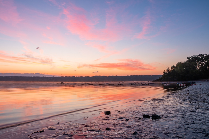 A photograph of dawn breaking over the Hudson River from along the shore of the Hudson River at Kingston Point Beach.