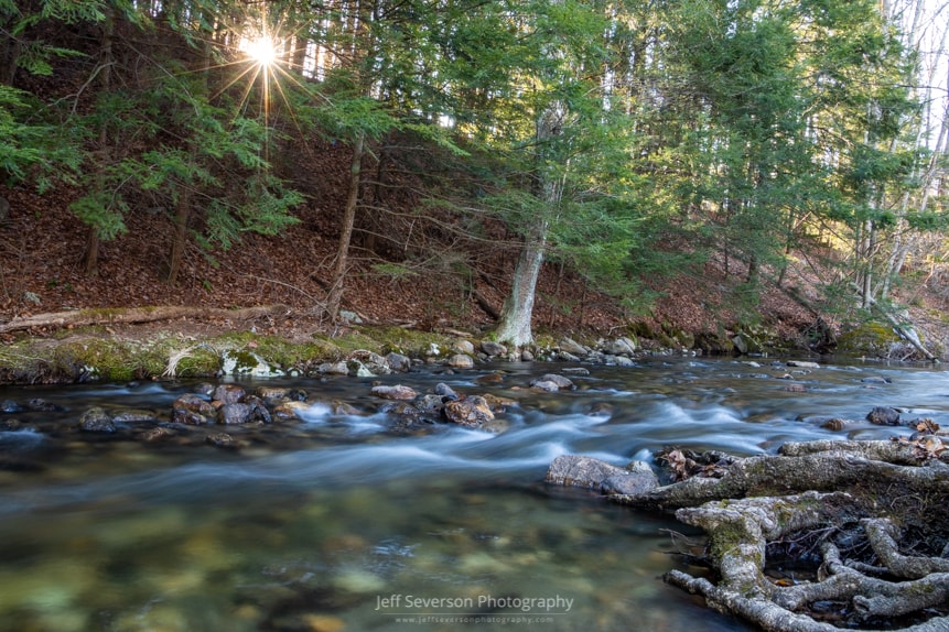A long exposure of water running on the Coxing Kill at Mohonk Preserve as the sun rises above the ridge.