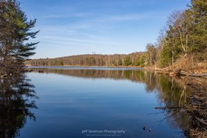 A landscape photo of Louisa Pond and surrounding tress reflected in it during an evening hike in March at Shaupeneak Ridge in Esopus, NY.