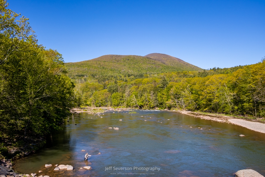 A photo from above the Esopus Creek on a May morning with a man fishing in the foreground and the Catskill Mountains in the background.