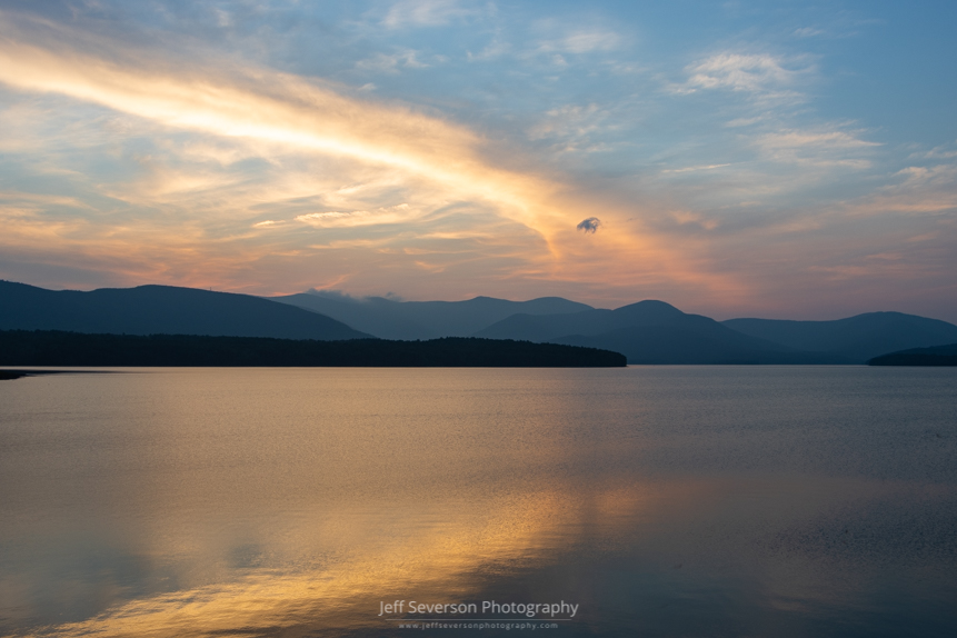 A photo of clouds reflected in the Ashokan Reservoir at sunset in August with the Catskill Mountains silhouetted in the background.