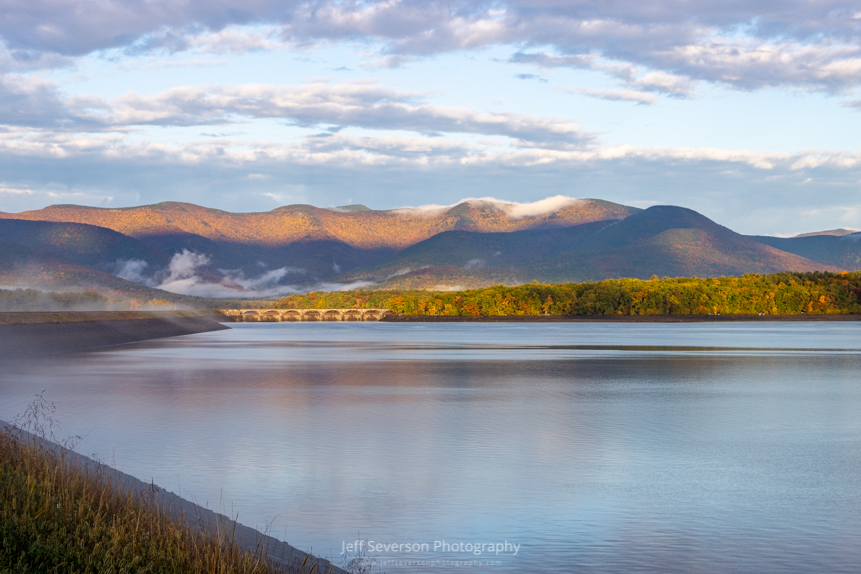 A photo of the lower basin of the Ashokan Reservoir as fog lifts during the beginning of the golden hour after sunrise on an October morning.