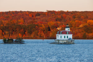 The golden hour before sunset turning the fall foliage on the east bank of the Hudson River behind the Esopus Lighthouse into to fiery reds and oranges.