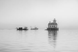 A black and white photo of a U.S. Coast Guard ship passing the Esopus Lighthouse as it travels South down the Hudson River on a foggy April morning.