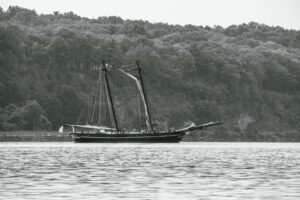 A black and white photo of The Amistad, a replica of a 19th century schooner, on the Hudson River as it waits to enter the Rondout Creek.