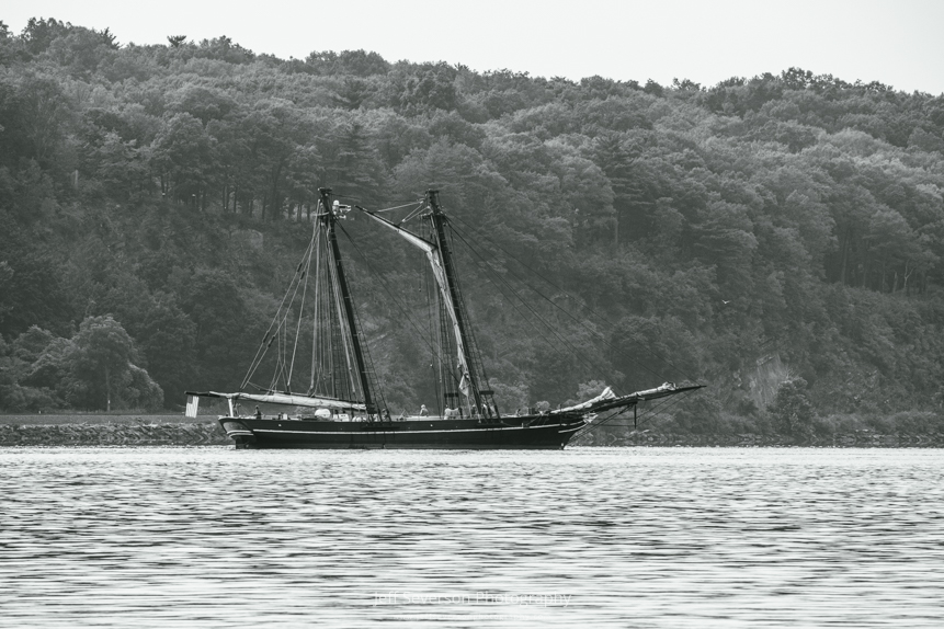 A black and white photo of The Amistad, a replica of a 19th century schooner, on the Hudson River as it waits to enter the Rondout Creek.