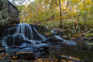 A long exposure photo of Middle Falls on Black Creek in Highland with the trees in the background covered in yellow fall foliage.