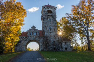 The sun shining through autumn foliage above Mohonk Preserve's Smiley Testimonial Gateway on an October morning.