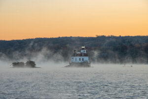 Autumn mist rising up off of the Hudson River at the Esopus Lighthouse as a lone fisherman fishes from a boat on an October morning.